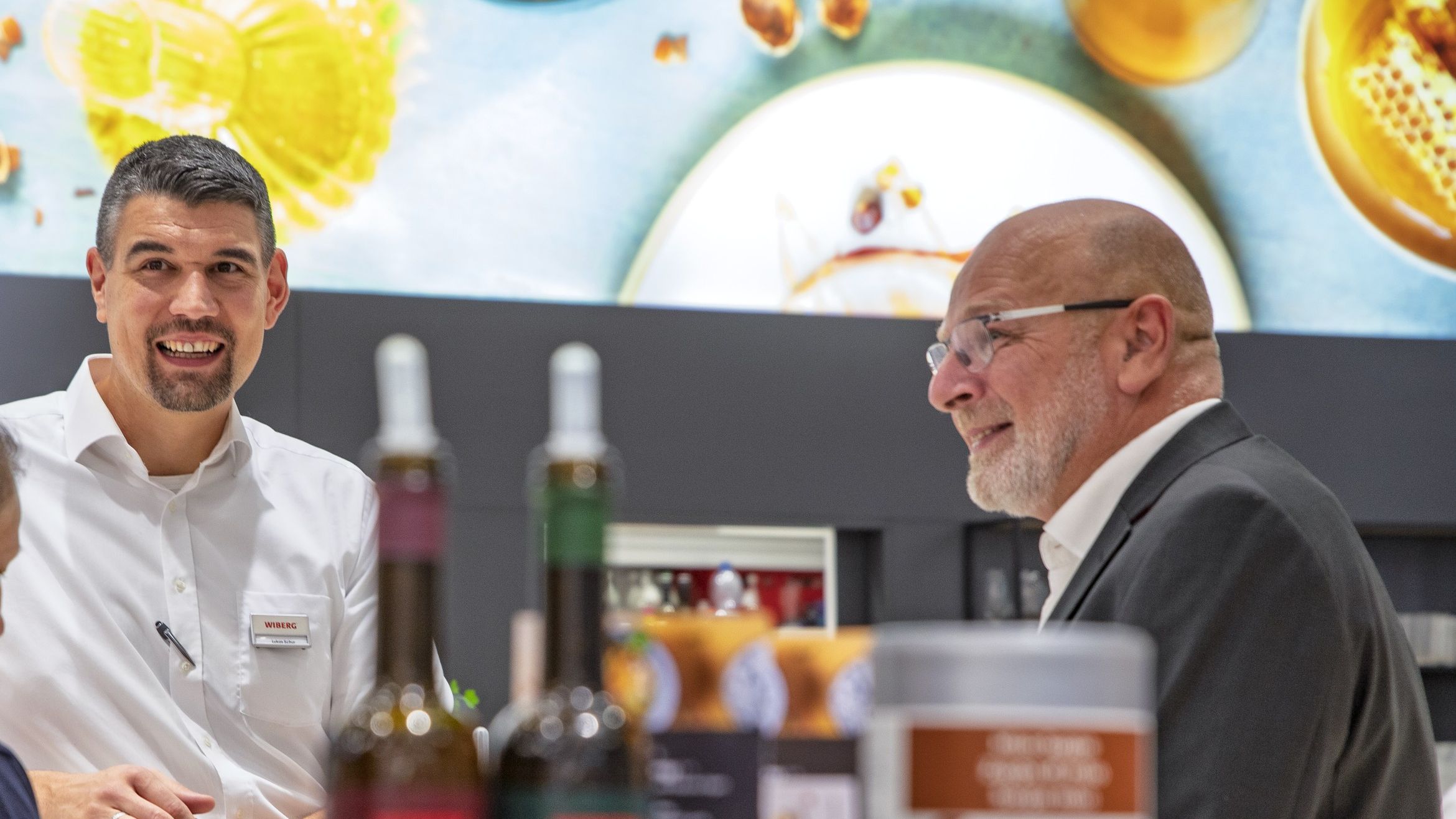 WIBERG Vertrieb auf dem WIBERG Messe-Stand, von vorne aufgenommen,  vor einem Leuchtbild mit neuen WIBERG Produkten auf einer Gastromesse.