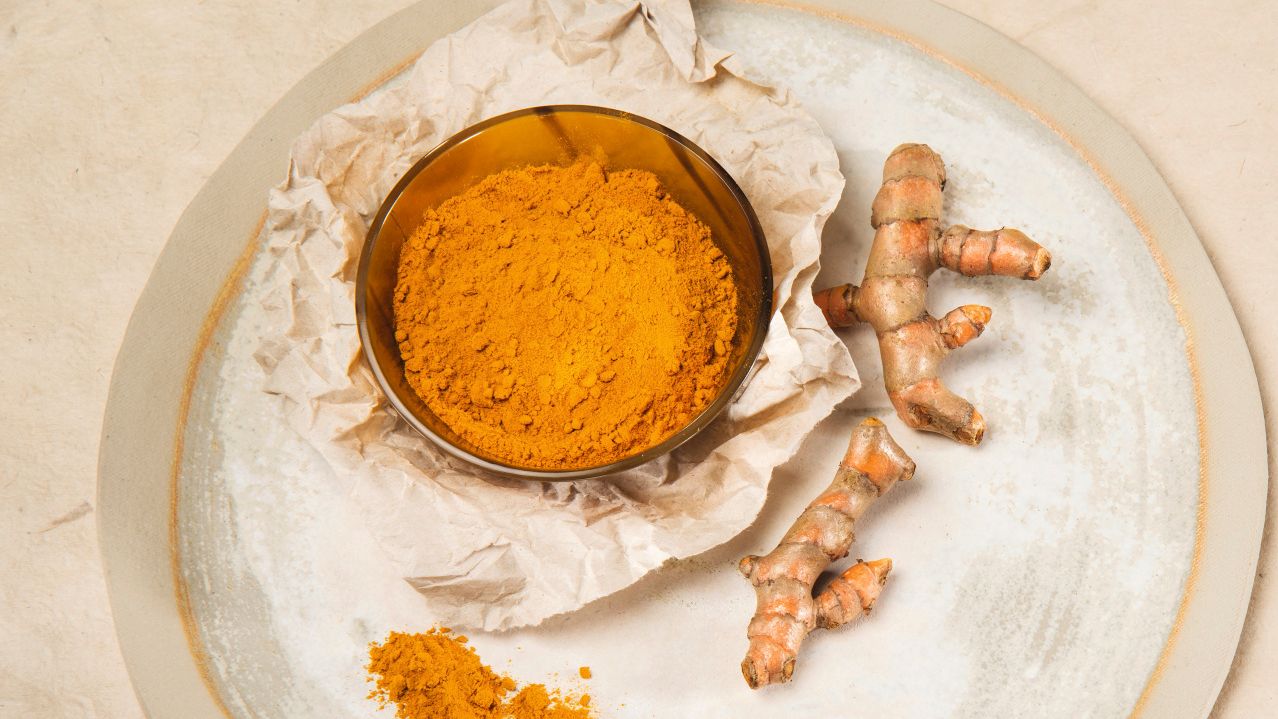 Gelbes Curcumapulver in einer Schale neben frischen Curcumawurzeln