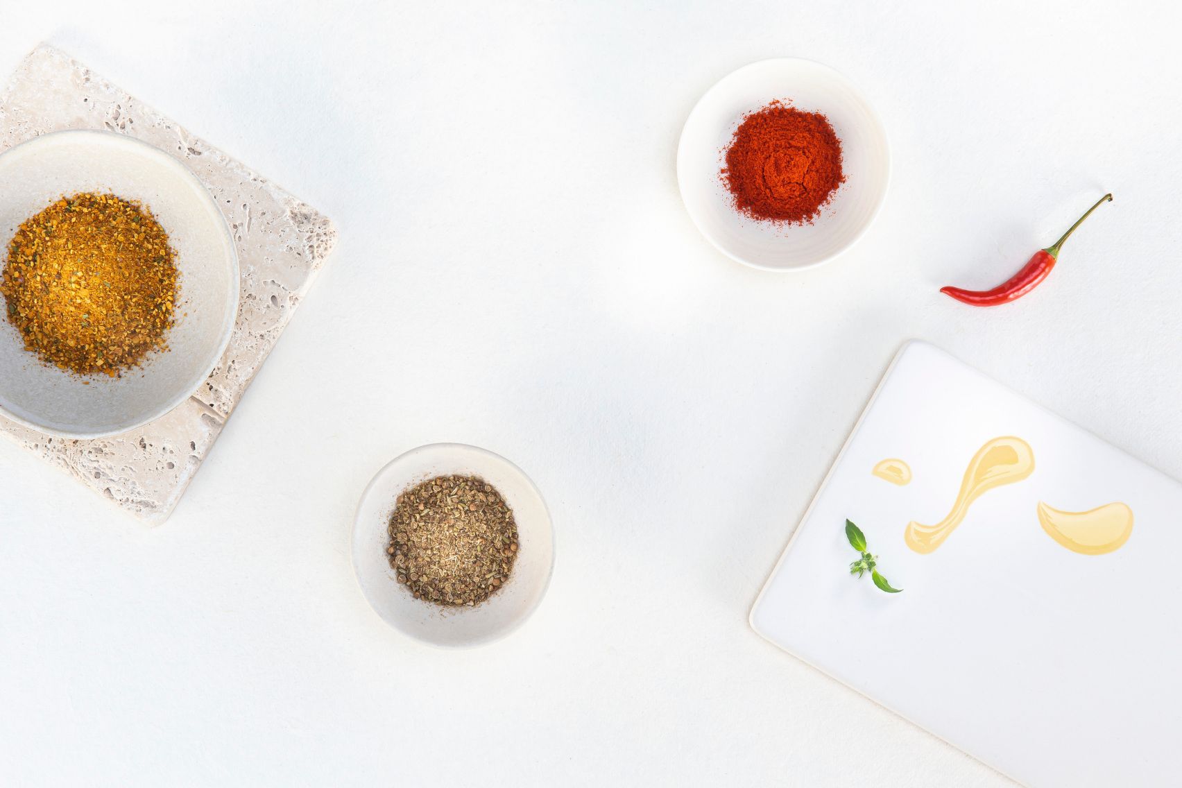 Rote und orange WIBERG Gewürzmischungen in Schüsseln mit Chilischote, frischen Kräutern und Öltropfen auf weißem Hintergrund – Aromenvielfalt für Profiköche.