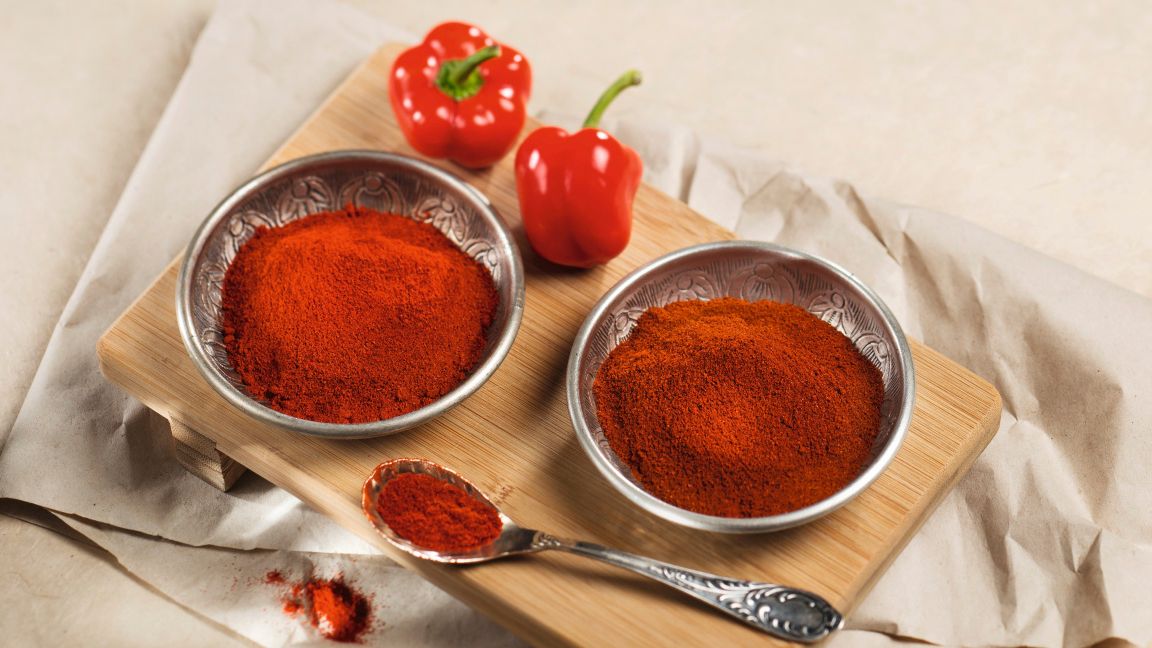 Rotes Paprikapulver in Metallschalen neben frischen roten Paprikaschoten