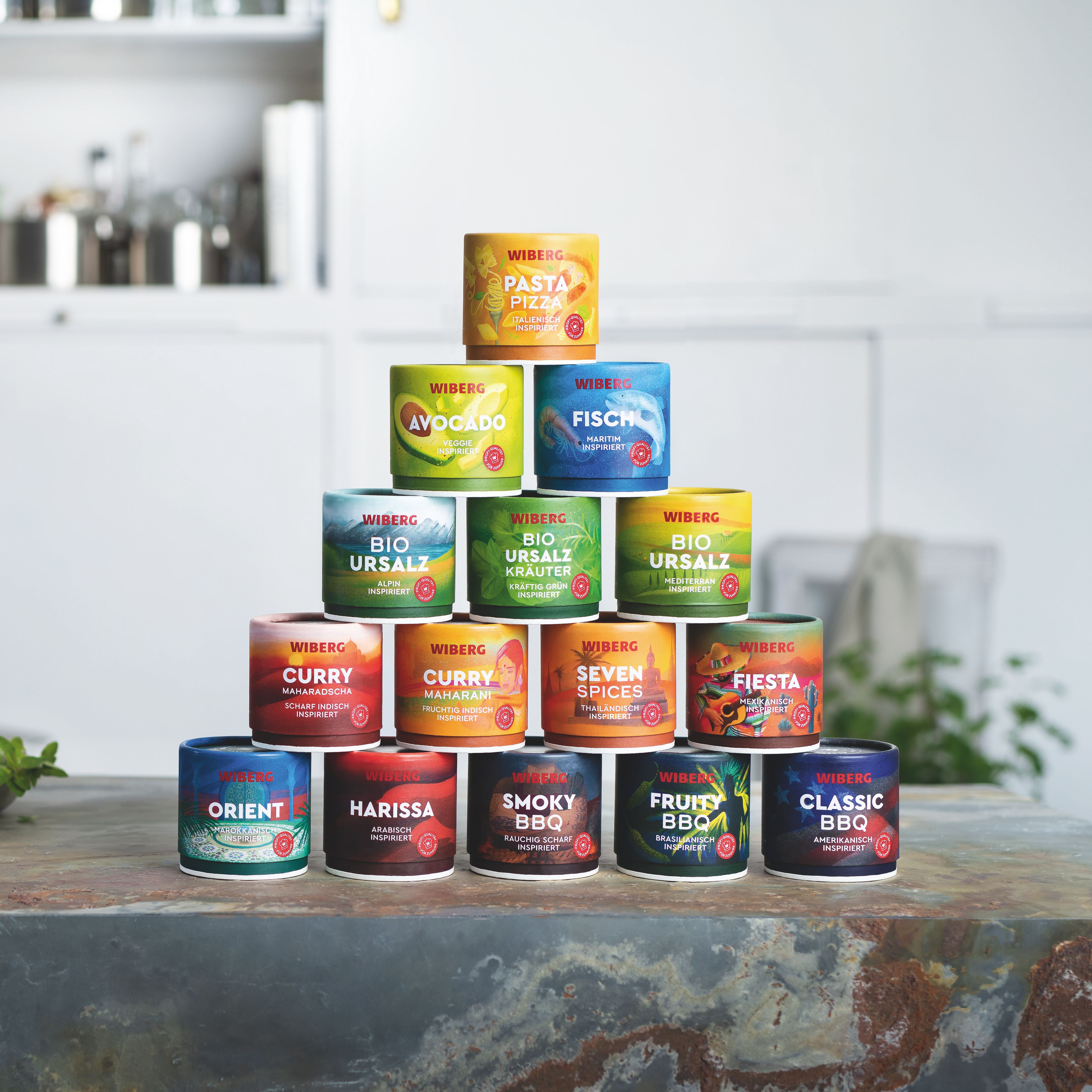 Pyramide aus 15 bunten WOW – World of WIBERG – Gewürzdosen in einer modernen hellen Küche, hochwertige Gewürzmischungen für zuhause.