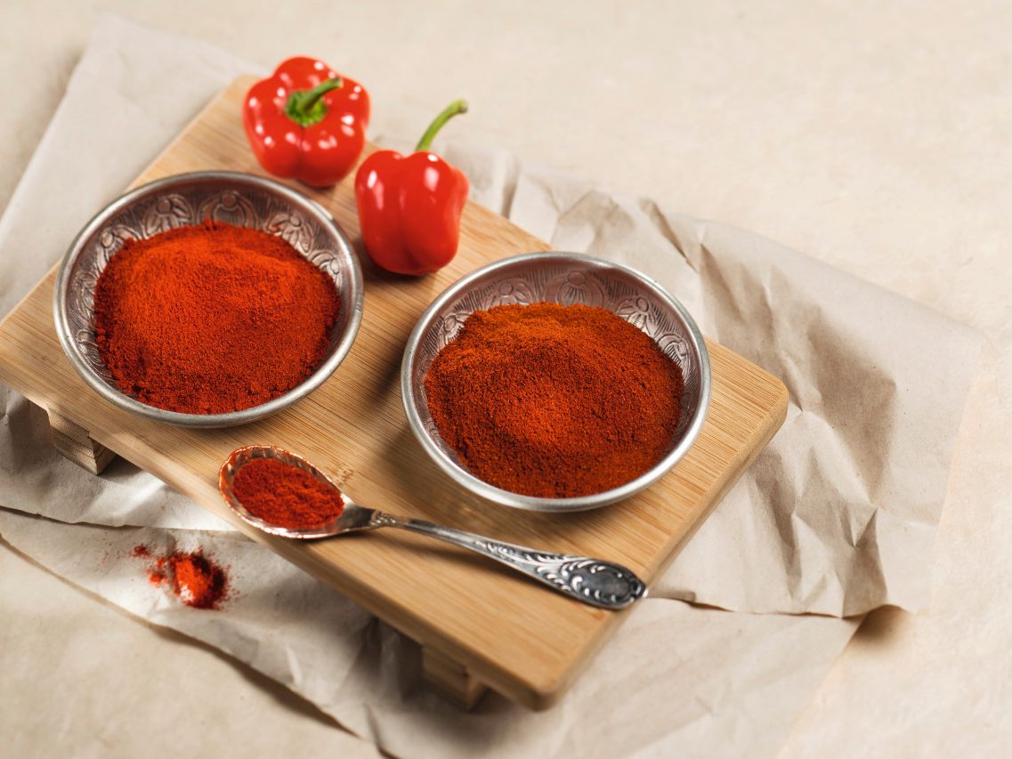 Rotes Paprikapulver in Metallschalen neben frischen roten Paprikaschoten