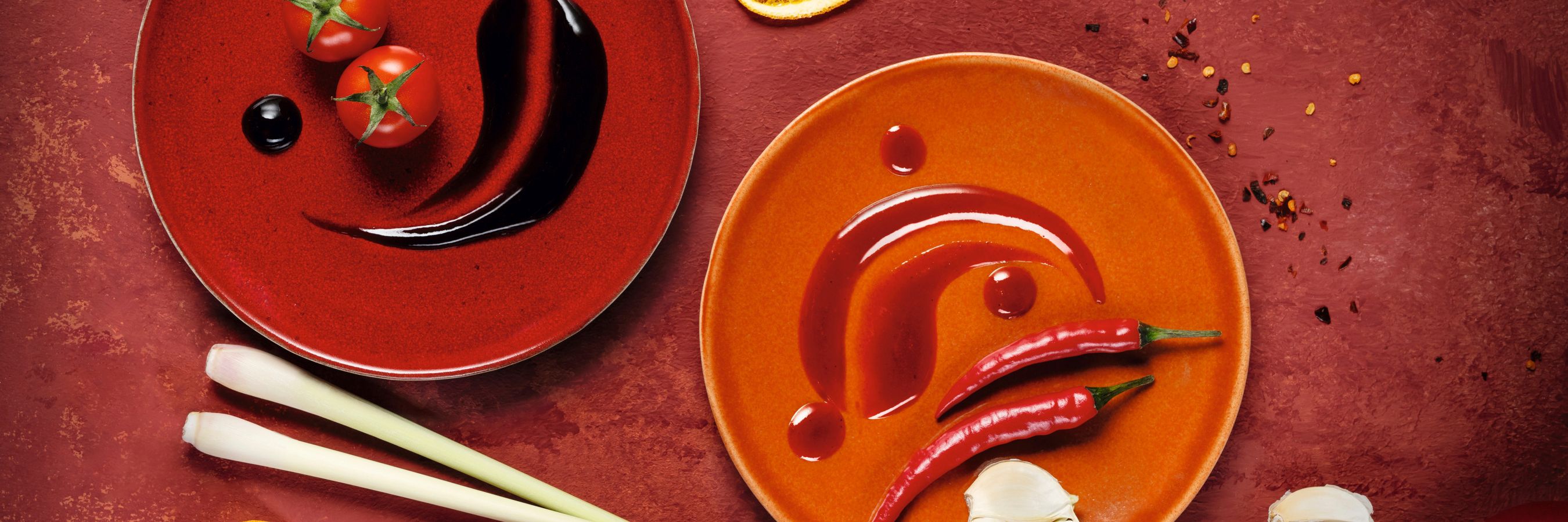WIBERG Würzsaucen Spicy Chili und Tasty Umami in Draufsicht, begleitet von frischen Chilis, Knoblauch und Tomaten – hochwertige Zutateninszenierung in Rot für Profiköche.