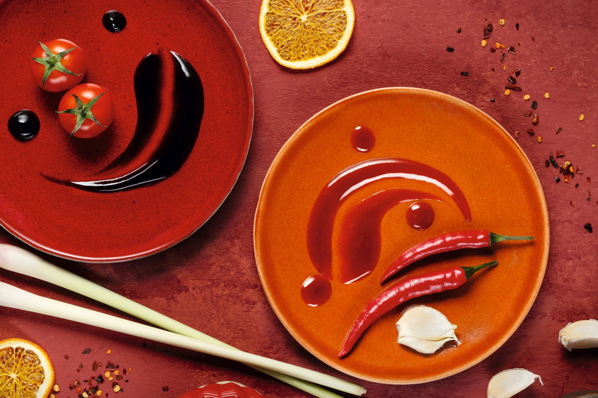 WIBERG Würzsaucen Spicy Chili und Tasty Umami in Draufsicht, begleitet von frischen Chilis, Knoblauch und Tomaten – hochwertige Zutateninszenierung in Rot für Profiköche.