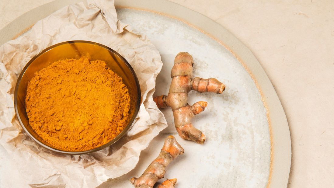 Gelbes Curcumapulver in einer Schale neben frischen Curcumawurzeln