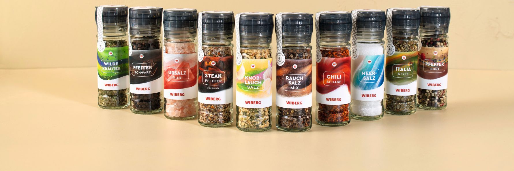 WIBERG Gewürzmühlen in halbkreisförmiger Anordnung: Wilde Kräuter, Pfeffer schwarz, Ursalz pur, Steak Pfeffer, Knoblauch‑Salz, Rauchsalz‑Mix, Chili scharf, Meersalz, Italia Style und Pfefferbunt.
