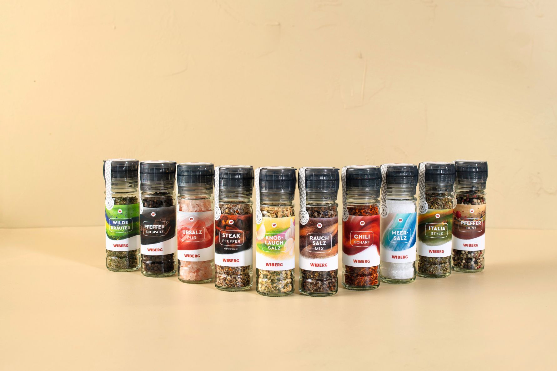 WIBERG Gewürzmühlen in halbkreisförmiger Anordnung: Wilde Kräuter, Pfeffer schwarz, Ursalz pur, Steak Pfeffer, Knoblauch‑Salz, Rauchsalz‑Mix, Chili scharf, Meersalz, Italia Style und Pfefferbunt.
