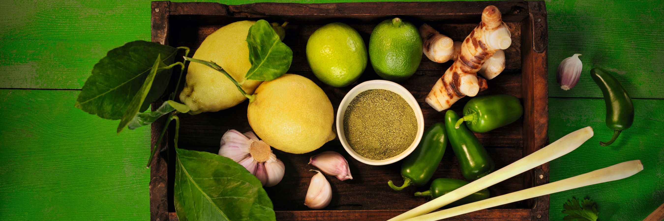 Querformat-Imagebild WIBERG Curry Grün auf strahlend grünem Hintergrund mit frischen Zutaten: Zitronen, Jalapeños, Kaffirlimette, Zitronengras, Ingwer, Knoblauch und Koriander – inspiriert von thailändischer Thai-Curry-Küche.