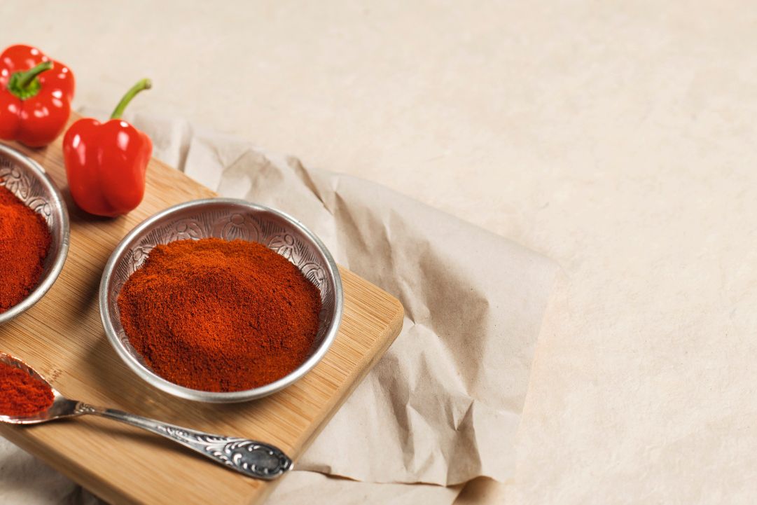 Rotes Paprikapulver in Metallschalen neben frischen roten Paprikaschoten