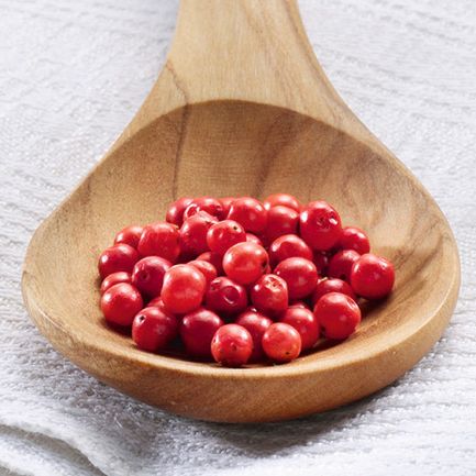 Rosa Pfefferbeeren auf einem Holzlöffel mit weißem Tuch und gelbem Hintergrund