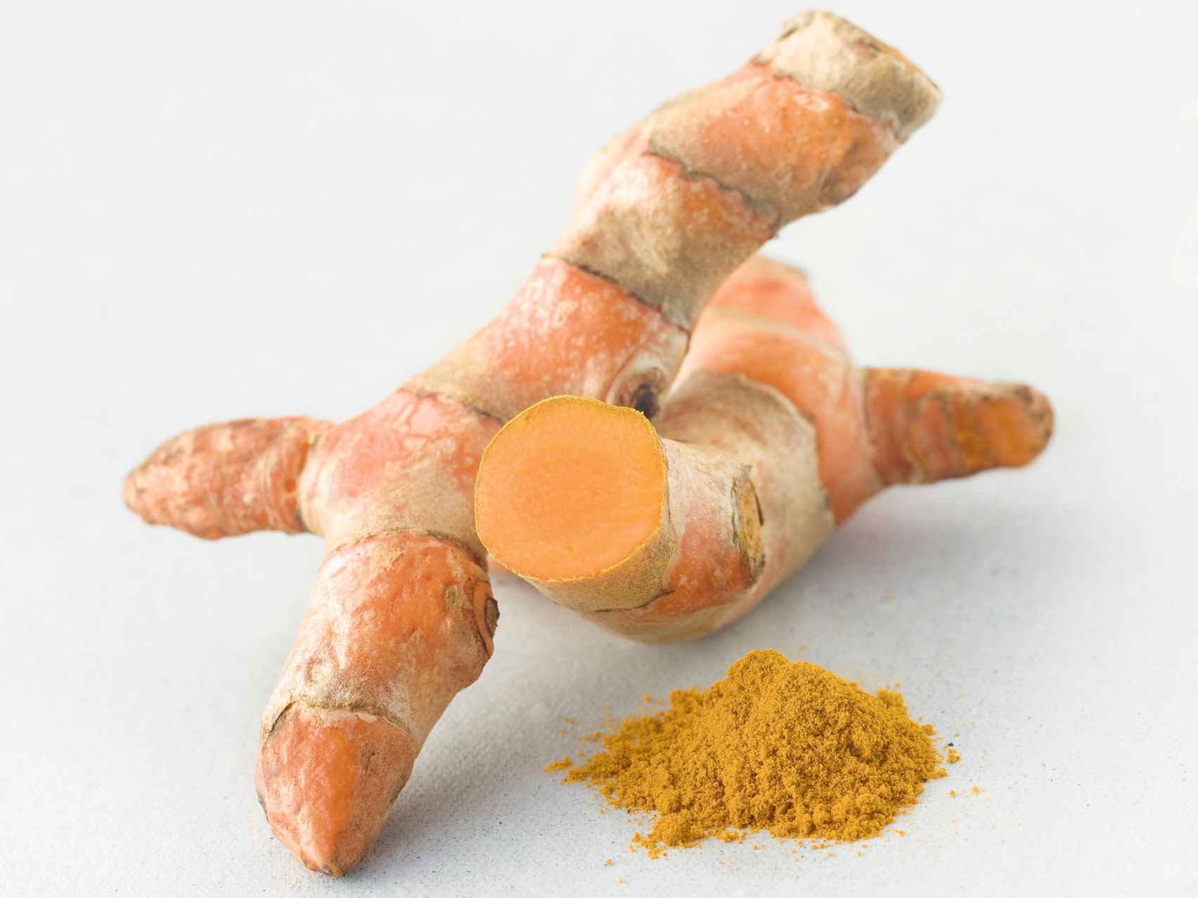 Curcumawurzeln und gelbes Curcumapulver vor weißem Hintergrund