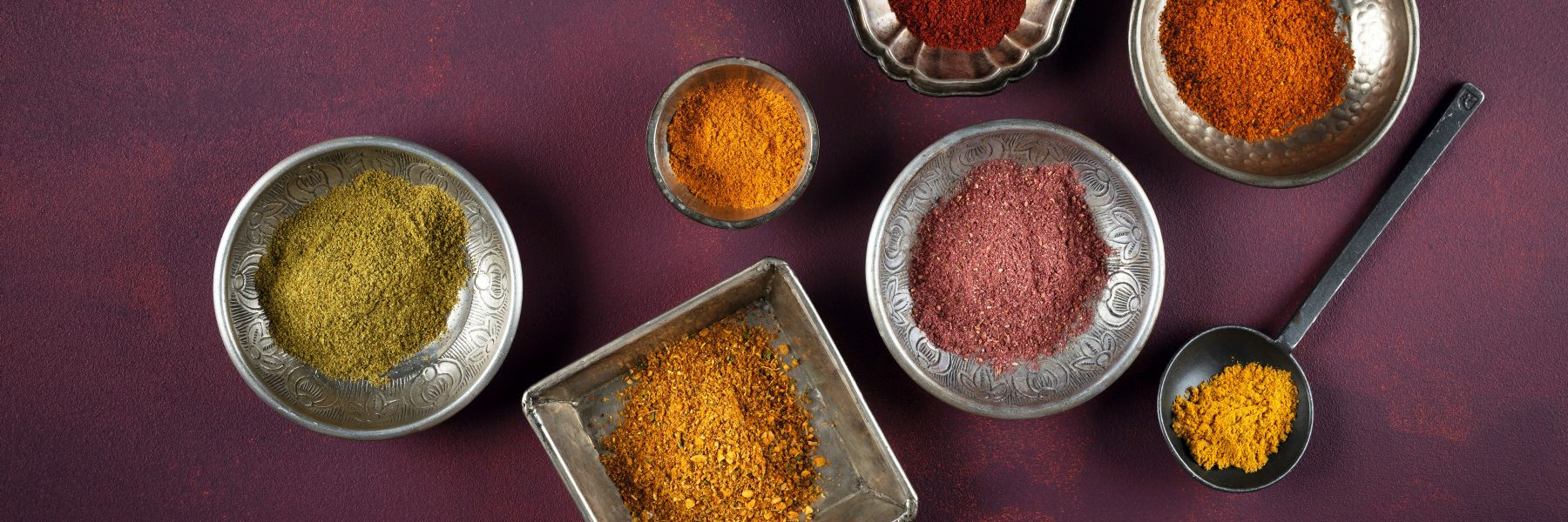 WIBERG Curry-Gewürzmischungen in orientalischen Schüsseln von oben: gelbe, grüne, orange, rote und purpurne Currys wie Curry Powder, Curry Grün, Curry Madrocas, Curry Orange, Curry Delhi, Curry Jaipur und Curry Purpur.