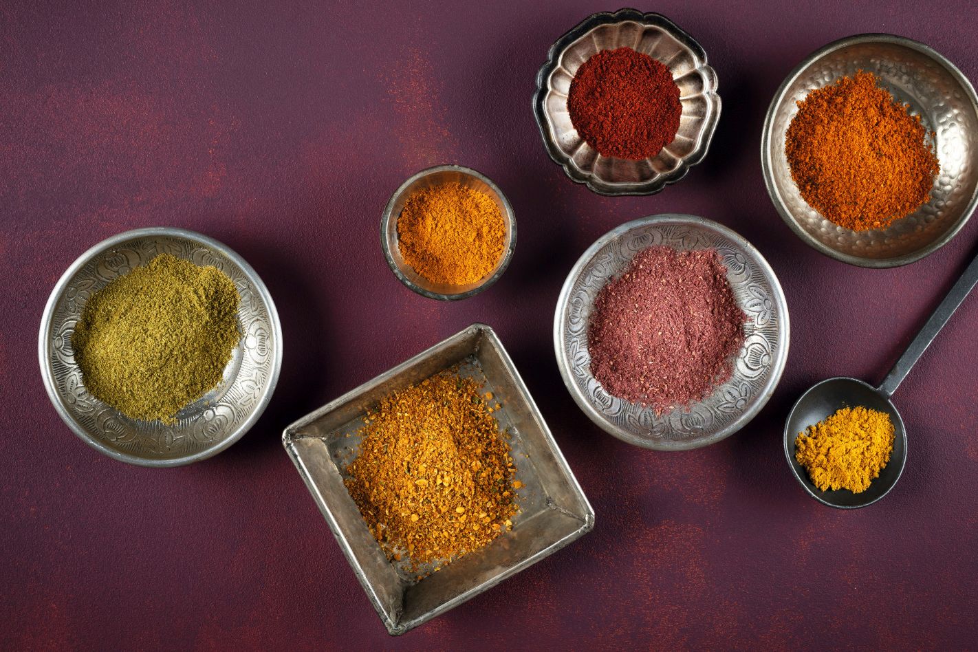 WIBERG Curry-Gewürzmischungen in orientalischen Schüsseln von oben: gelbe, grüne, orange, rote und purpurne Currys wie Curry Powder, Curry Grün, Curry Madrocas, Curry Orange, Curry Delhi, Curry Jaipur und Curry Purpur.
