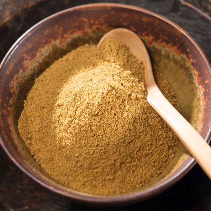 Gemahlener Kreuzkümmel in einer dunklen Schale mit kleinem Holzlöffel