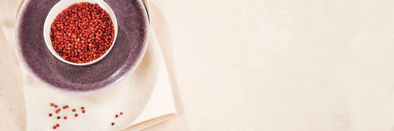 Rosa Pfefferkörner in einer weißen Schale auf einem violetten Teller