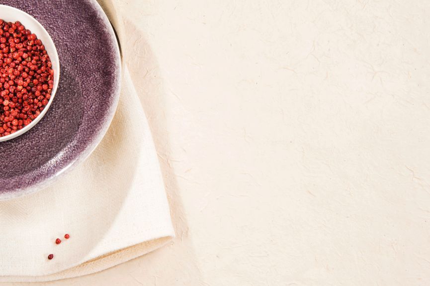 Rosa Pfefferkörner in einer weißen Schale auf einem violetten Teller