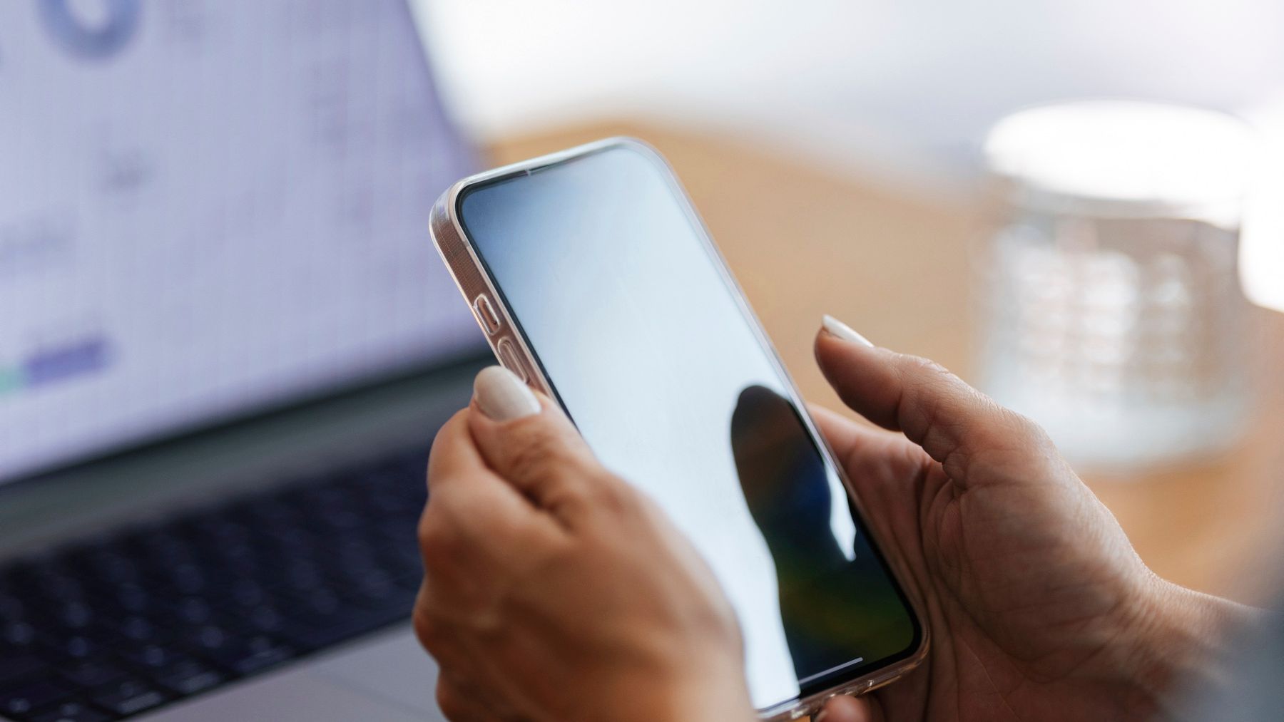 Aufgeklappter Laptop im Hintergrund und Hände mit Smartphone im Vordergrund – Symbolbild für die digitalen Kontaktmöglichkeiten zu NovaTaste.