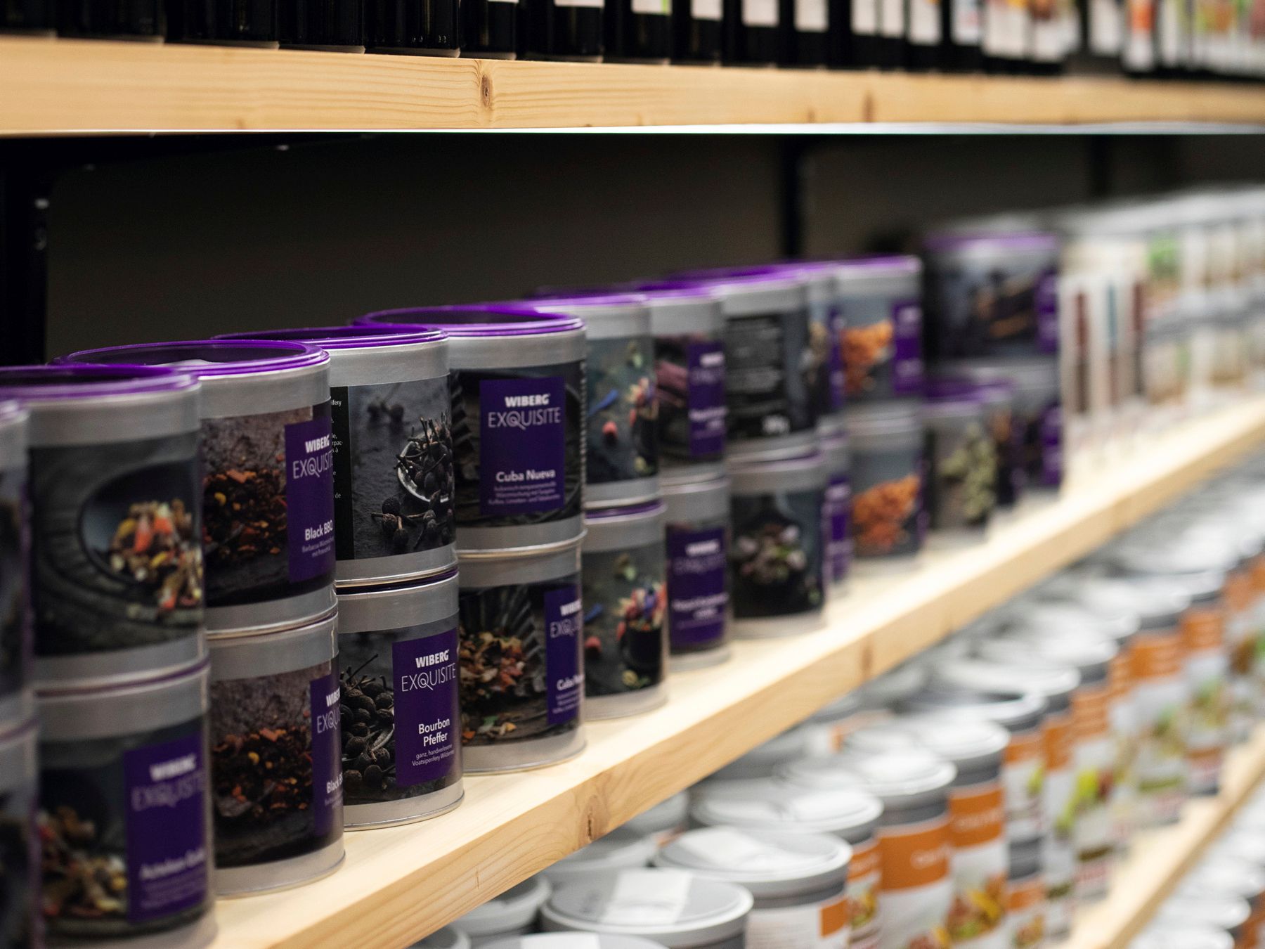 Regal mit WIBERG Exquisite Aromatresor‑Dosen, das von links nach rechts perspektivisch verläuft und am rechten Bildrand in die Unschärfe übergeht – Symbol für Produktvielfalt und Tiefe.