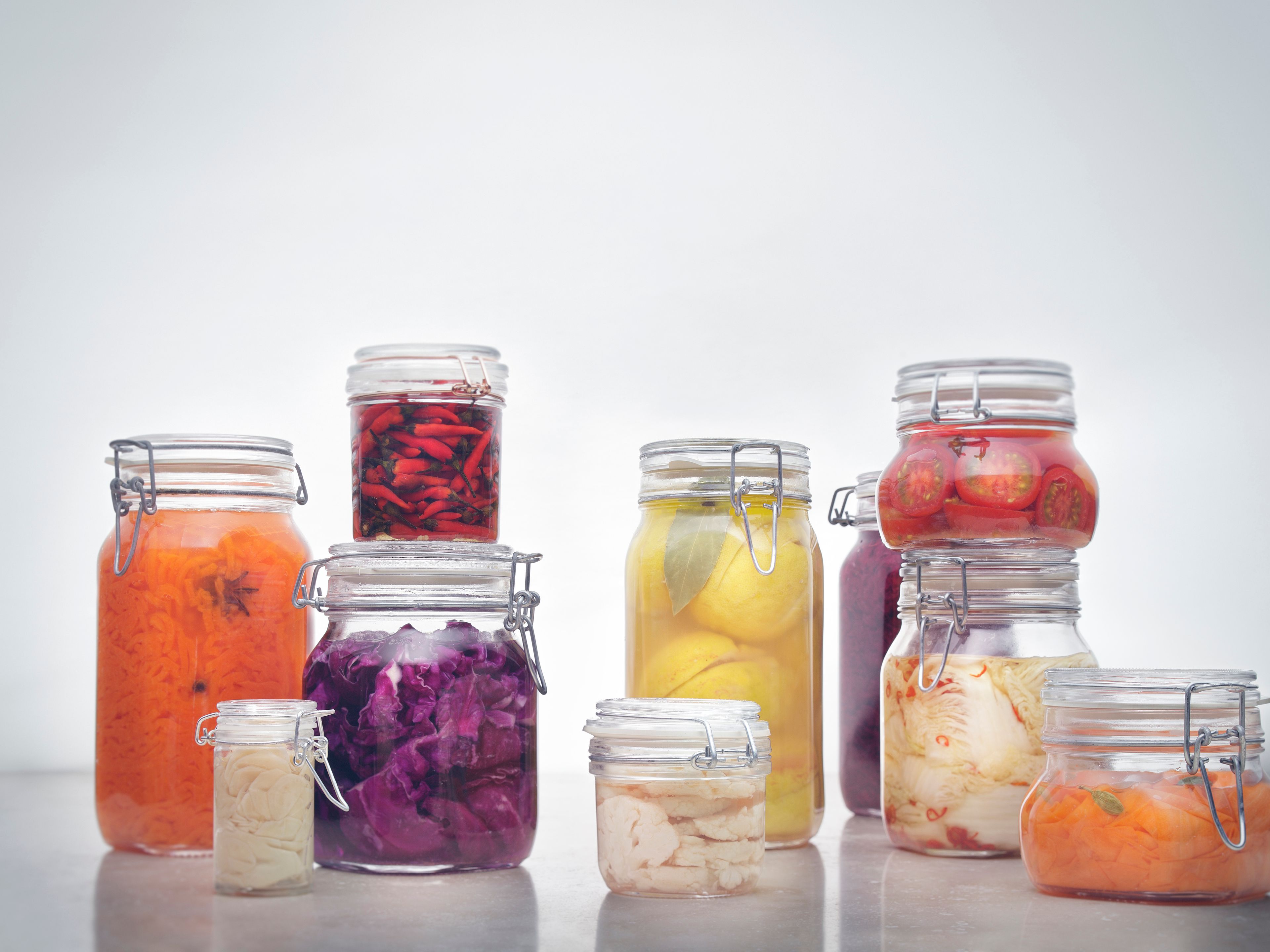 Zehn unterschiedlich große Einmachgläser mit in Essig fermentiertem Gemüse wie Karotten, Chilis, Rotkraut, Zitronen, Kraut, Tomaten und Blumenkohl in orange, rot, lila, gelb und weiß auf hellem grauem Hintergrund; Bildmotiv von WIBERG für Profiköche.