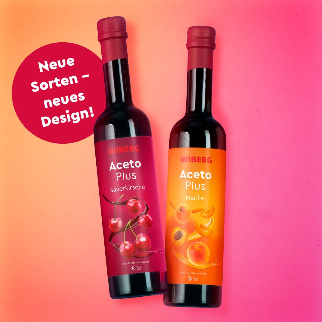 WIBERG AcetoPlus Sauerkirsche und WIBERG AcetoPlus Marille – Essig‑Fruchtzubereitungen in dunklen 500‑ml‑Flaschen mit modernem kirschrotem bzw. orangem Etikett vor apricot‑pinkem Farbverlauf und dunkelroter Bubble mit dem Text ‚neue Sorten – neues Design‘.