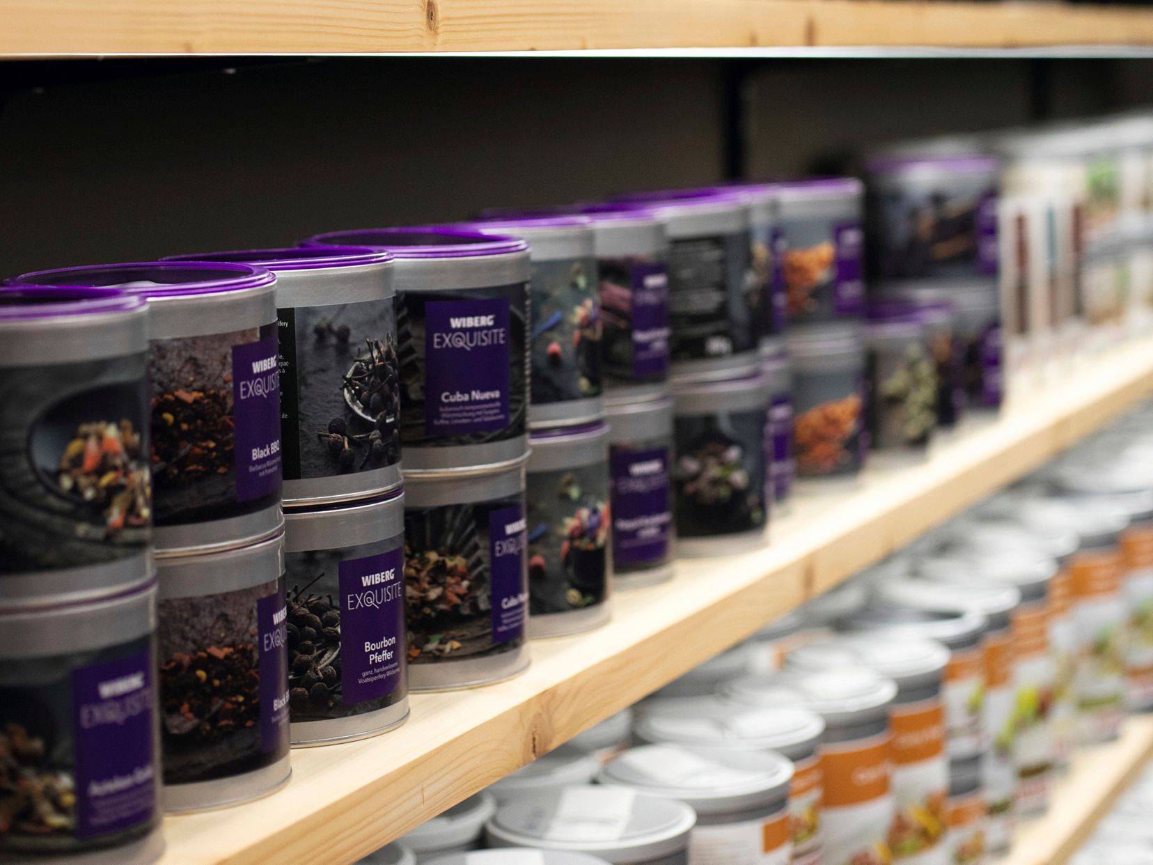 Regal mit WIBERG Exquisite Aromatresor‑Dosen, das von links nach rechts perspektivisch verläuft und am rechten Bildrand in die Unschärfe übergeht – Symbol für Produktvielfalt und Tiefe.