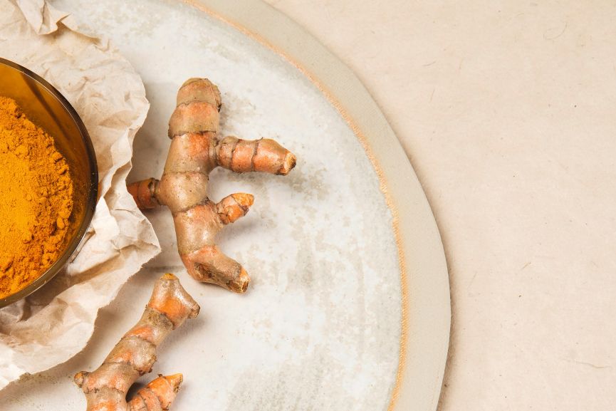 Gelbes Curcumapulver in einer Schale neben frischen Curcumawurzeln
