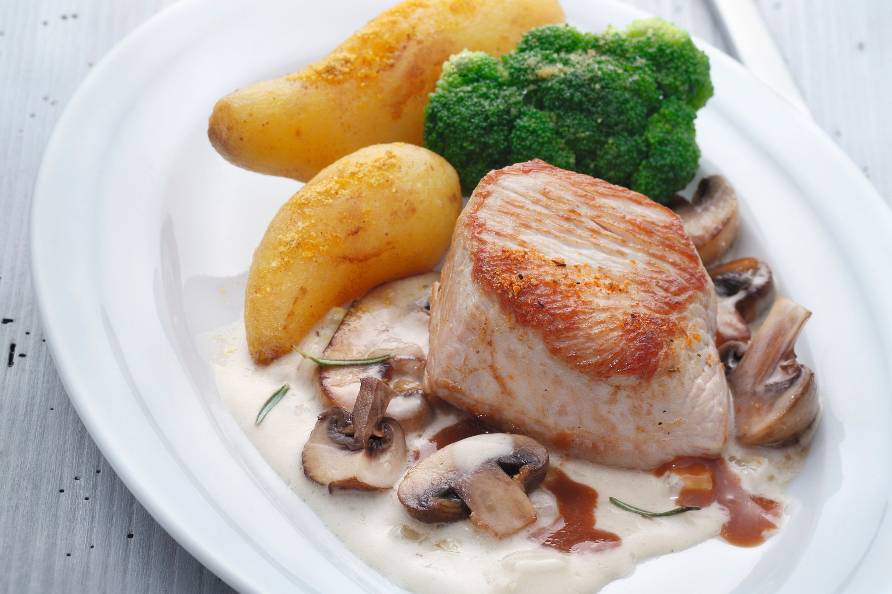 Heller Teller mit gebratenem Putensteak, Rahm-Pilzen, knusprigen Bratkartoffeln und Brokkoli – angerichtet mit WIBERG Gewürzen für die Profi-Küche.