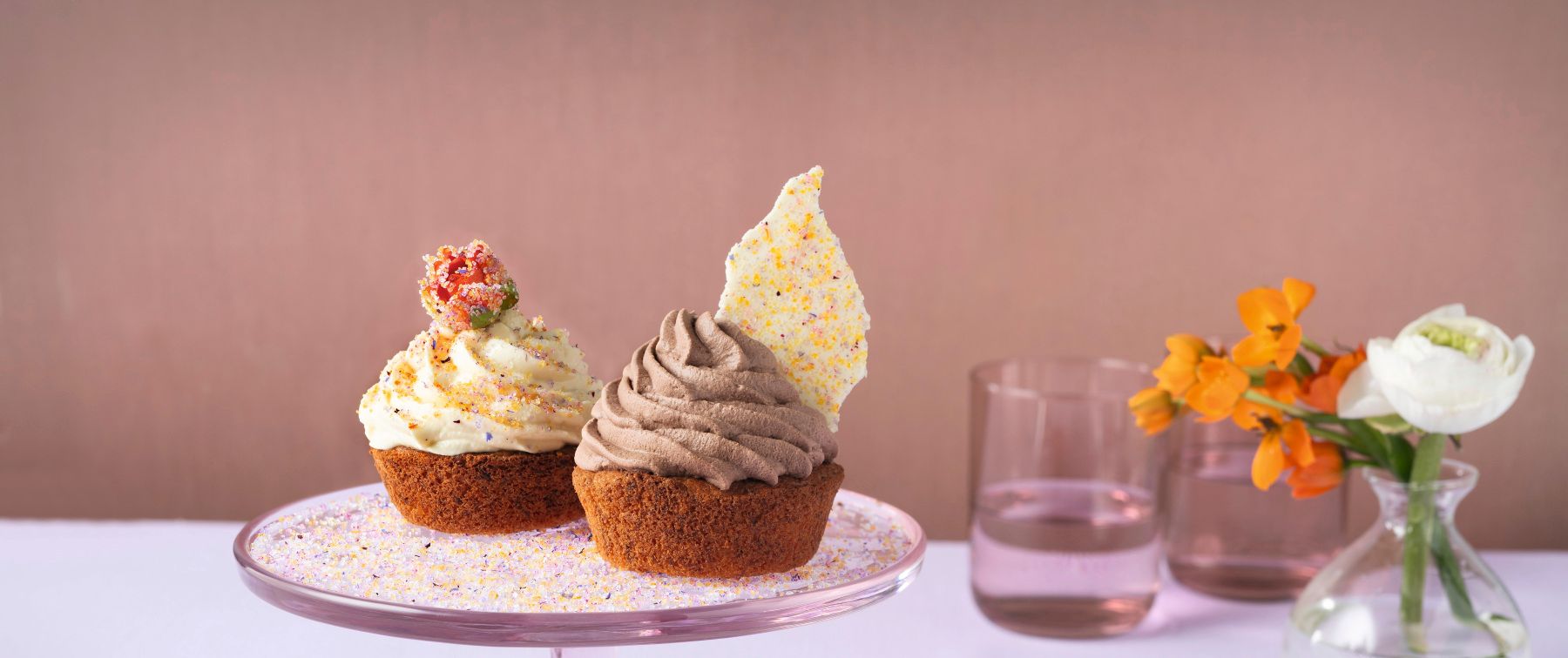 WIBERG Blütenzucker bunt in Rosa, Lila, Gelb und Orange – gestreut über Karotten‑Schokoladen‑Cupcakes mit Mangofüllung, Schokoladen‑ und Mango‑Frosting sowie Schokoladen‑Blütenzucker‑Chips.