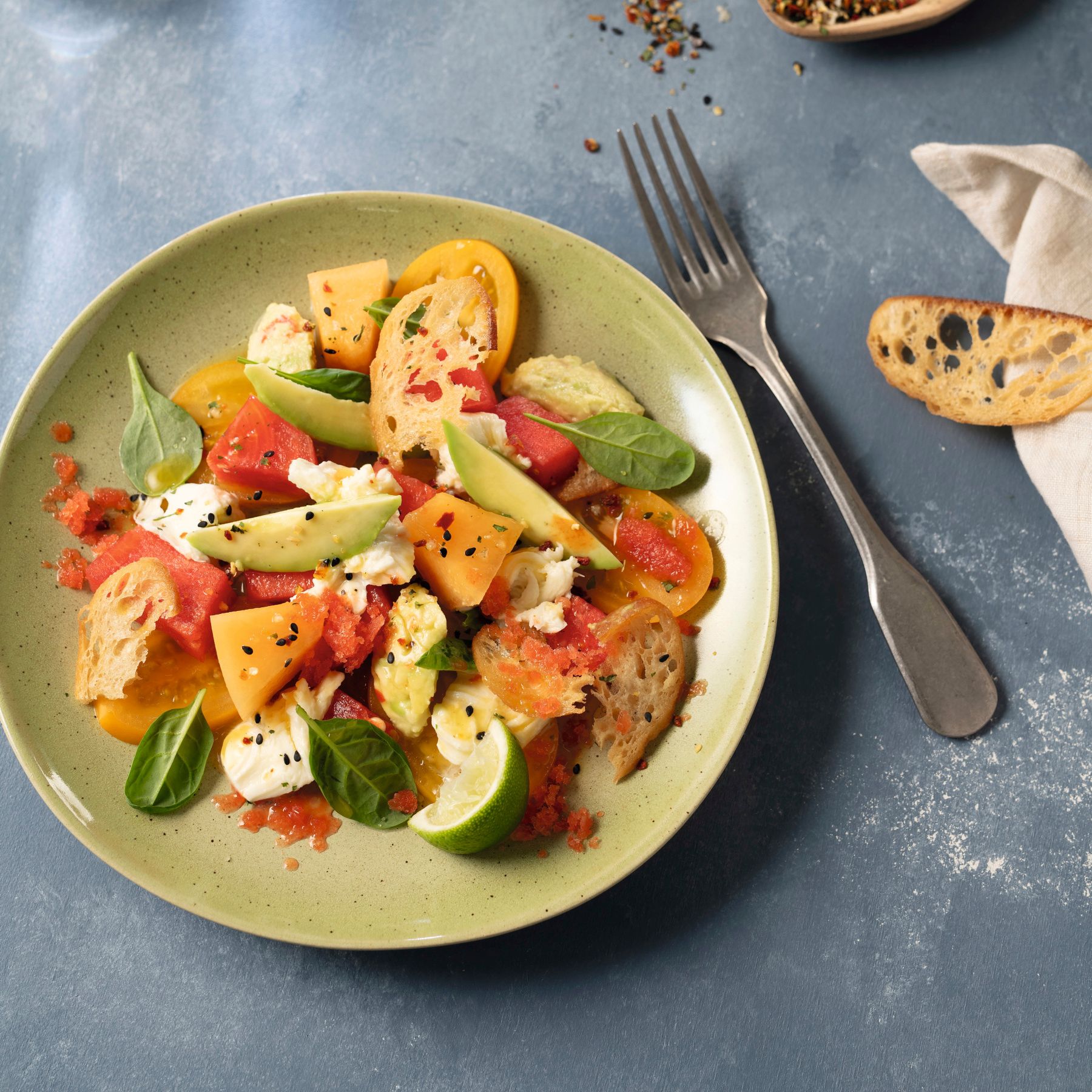 Bunter Avocado-Salat mit Büffelmozzarella und geeistem Melonen-Dressing auf frühlingshaftem Hintergrund – verfeinert mit WIBERG Gewürzen und Spezialitäten für Profiköche.