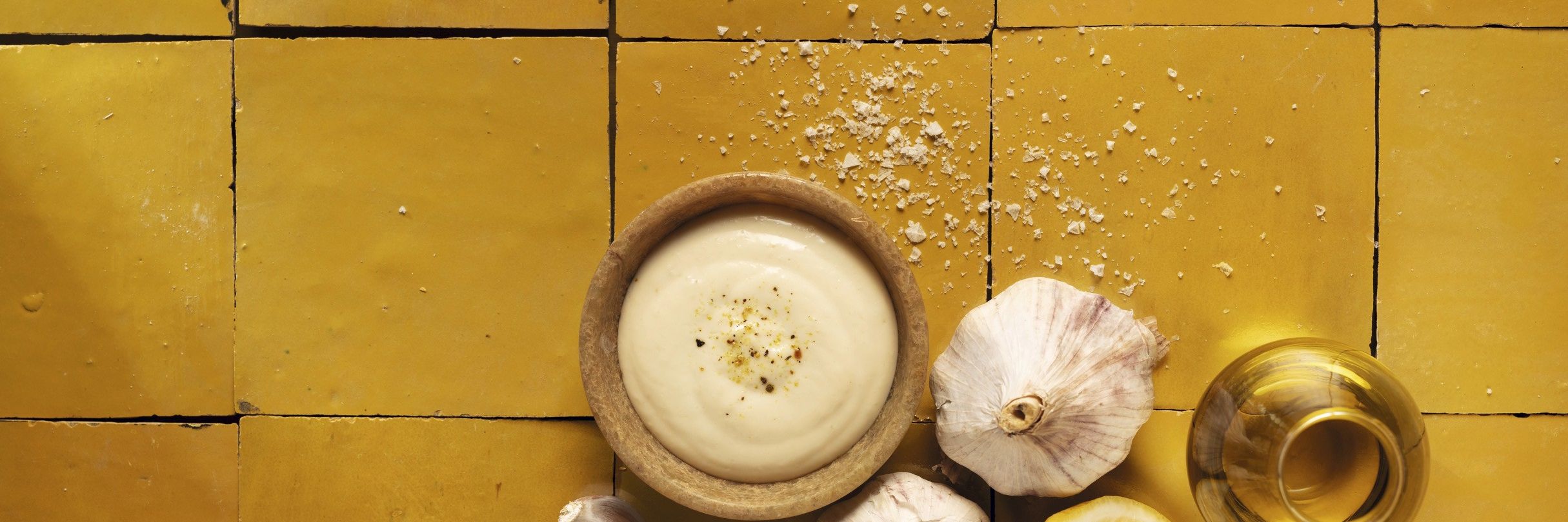 Cremige WIBERG Aioli in Schüssel, daneben frischer Knoblauch, Zitrone, Salz und Olivenöl, von oben fotografiert – hochwertige Zutaten für Profiköche.