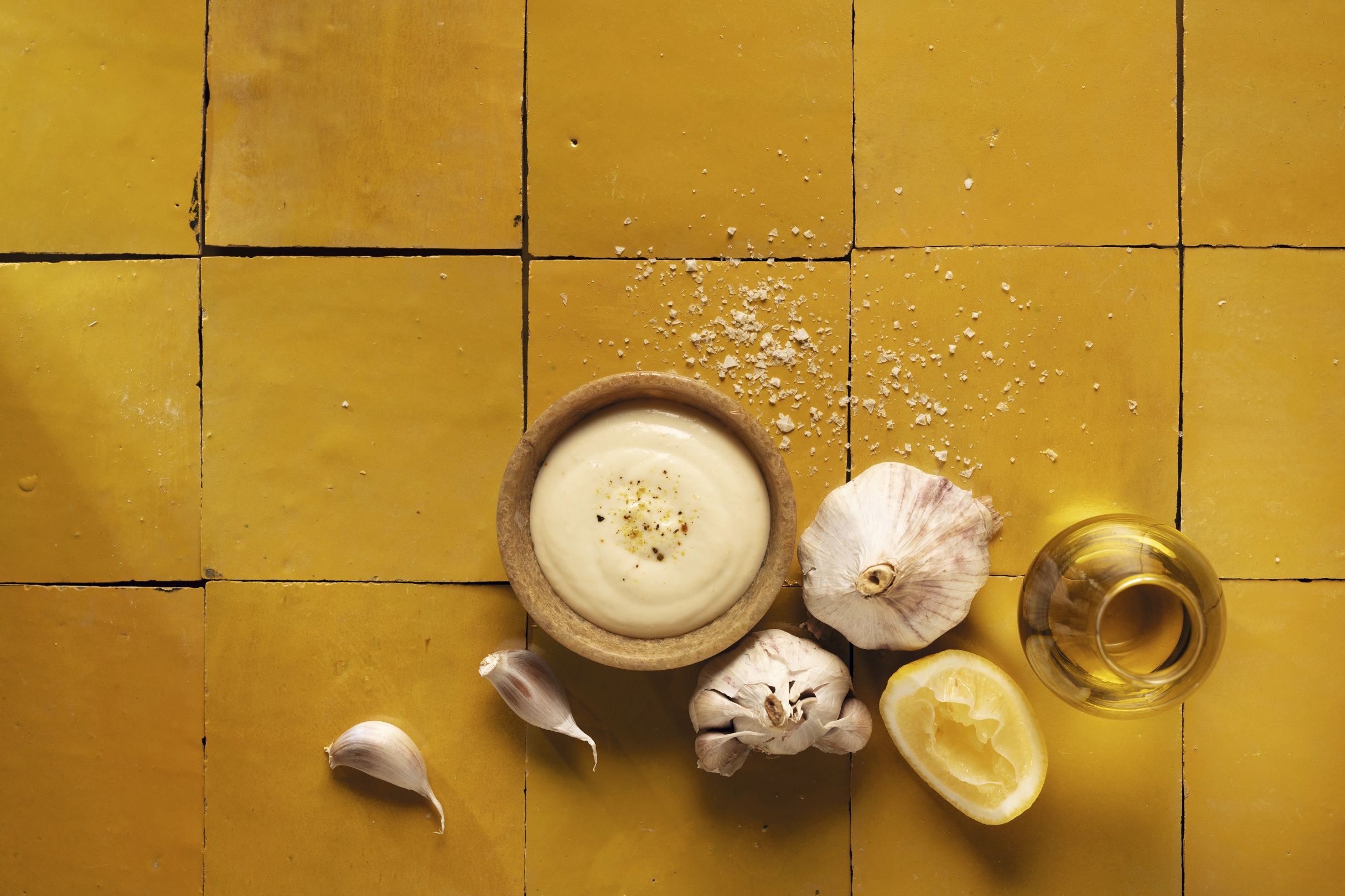 Cremige WIBERG Aioli in Schüssel, daneben frischer Knoblauch, Zitrone, Salz und Olivenöl, von oben fotografiert – hochwertige Zutaten für Profiköche.