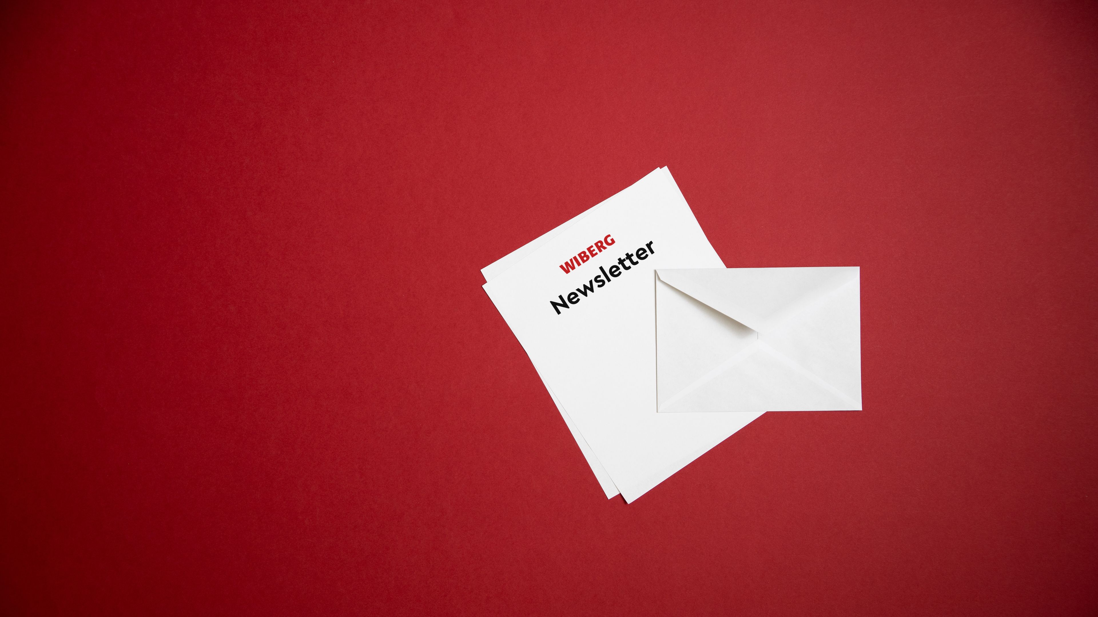 Spotlight auf einen weißen Brief mit rotem WIBERG Logo und der Aufschrift „Newsletter“, dazu ein weißes Kuvert vor dunkelrotem Hintergrund.