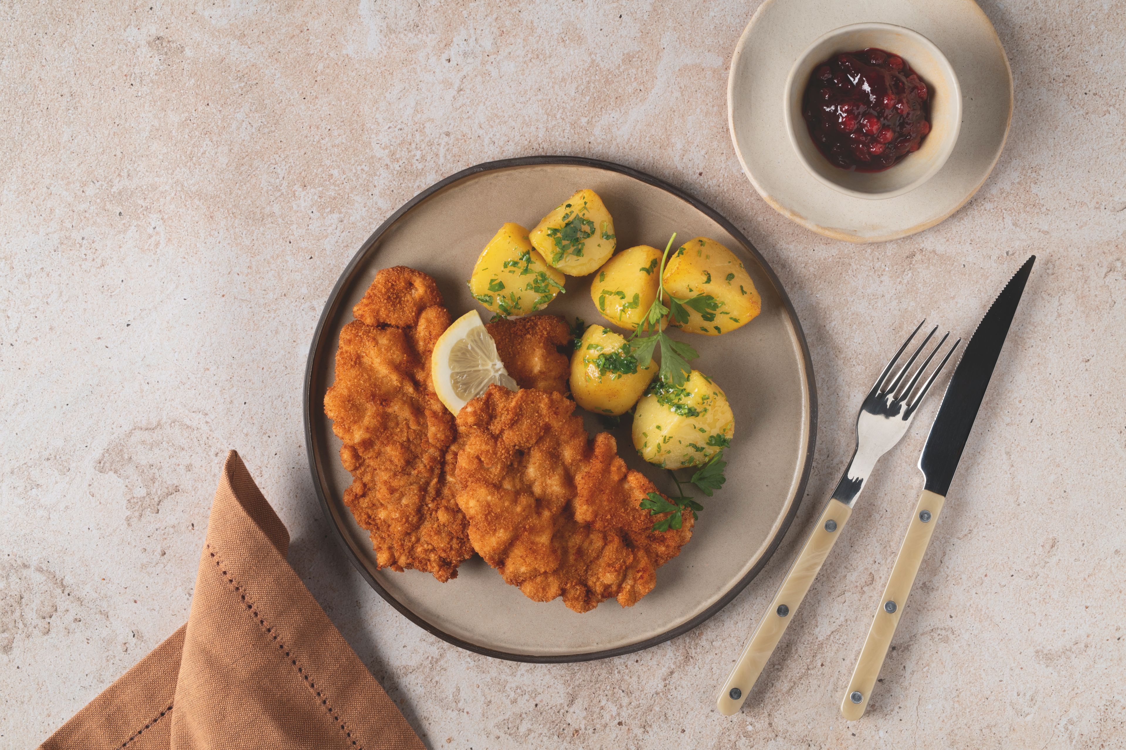 Panierte Schnitzel mit Petersilienkartoffeln, Zitrone und Preiselbeeren auf einem Teller