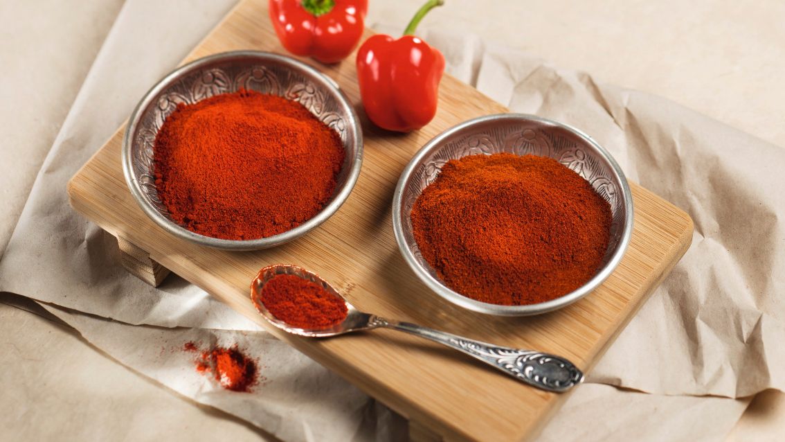 Rotes Paprikapulver in Metallschalen neben frischen roten Paprikaschoten