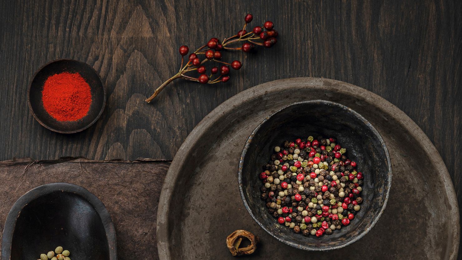 Von oben fotografiertes, dunkles und stimmungsvolles WIBERG Bild mit verschiedenen Gewürzen, u.a. Paprika, bunter Pfeffer, Kardamom, Langpfeffer, Tomatenflocken und Muskat.