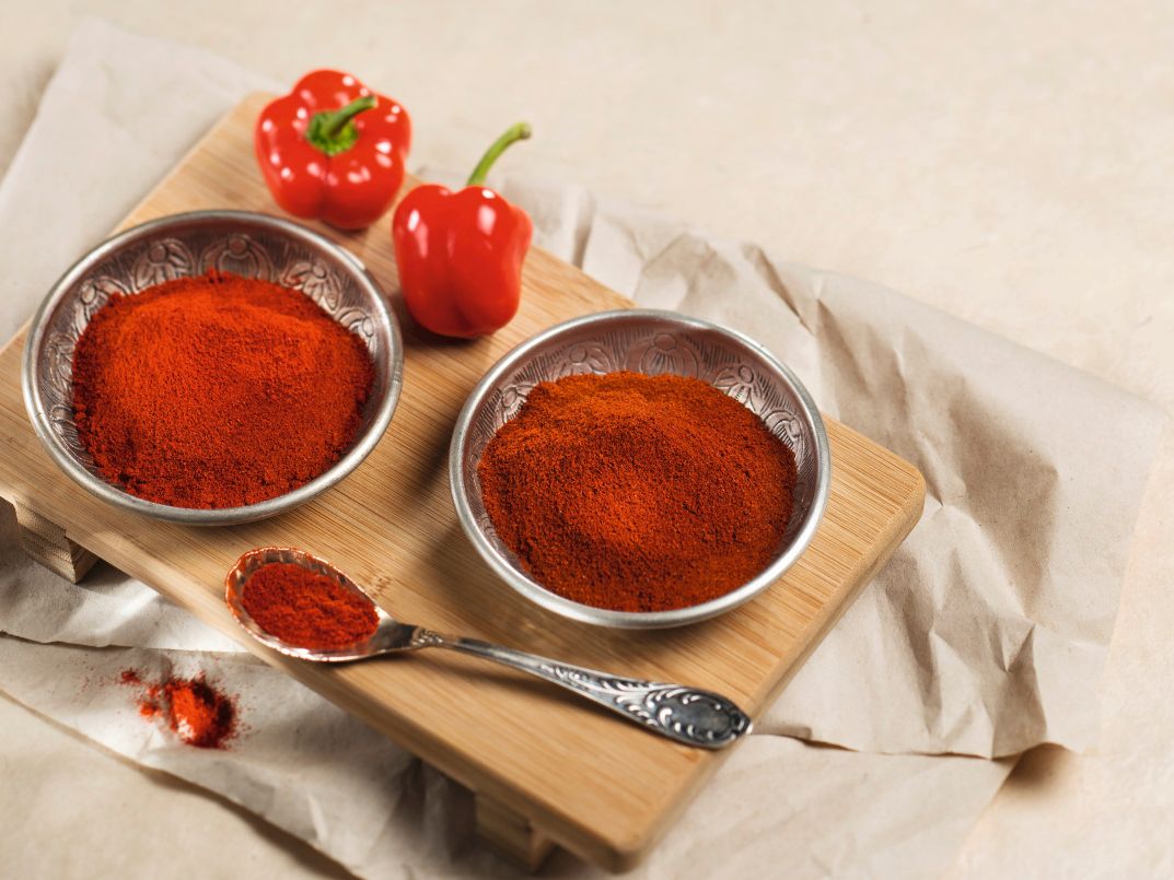 Rotes Paprikapulver in Metallschalen neben frischen roten Paprikaschoten