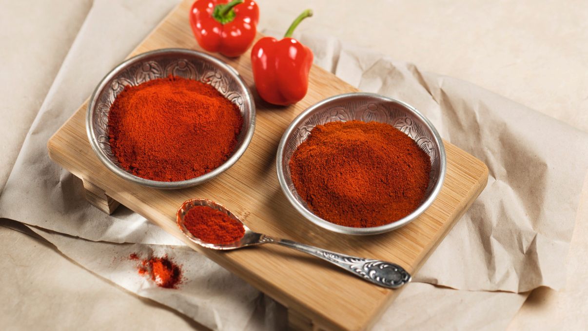Rotes Paprikapulver in Metallschalen neben frischen roten Paprikaschoten