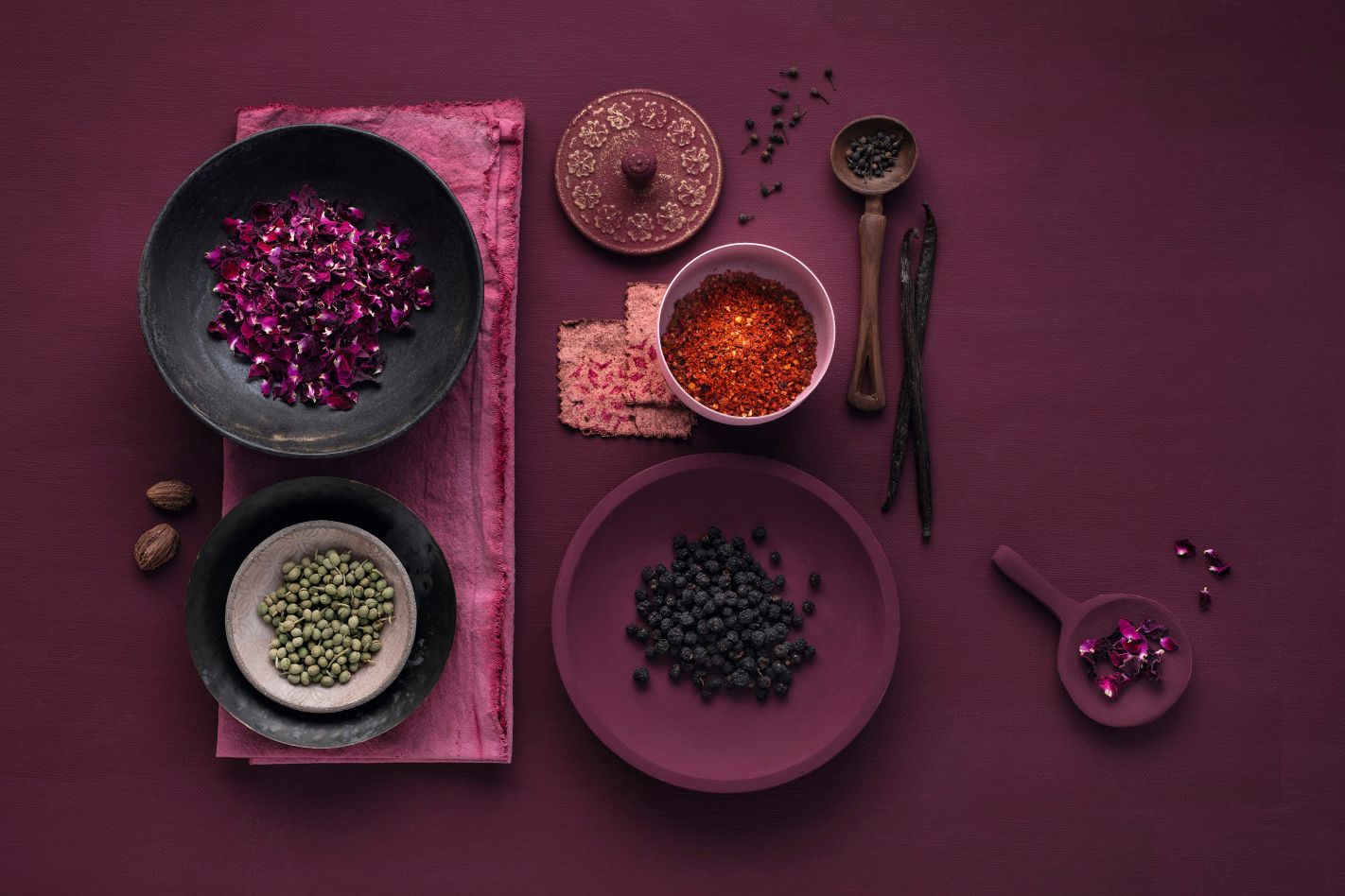 WIBERG Exquisite Produkte in Schüsseln und Tellern vor magentafarbenem Hintergrund: Rosenblüten, rote Gewürzmischung, edler Pfeffer und Vanilleschoten – Premiumaromen für Profiköche.